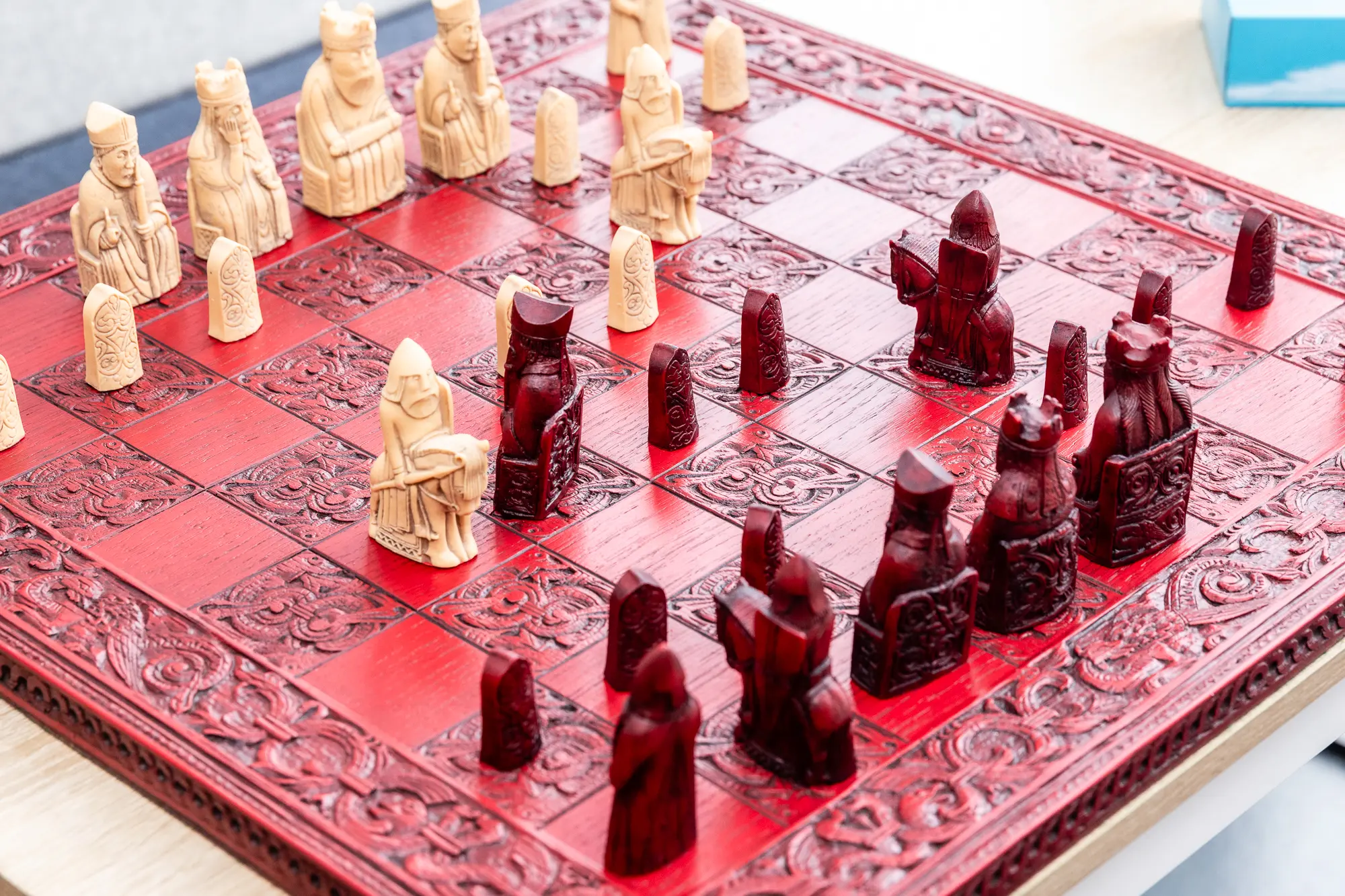Ornate carved wooden chessboard with detailed beige and dark red chess pieces mid-game.