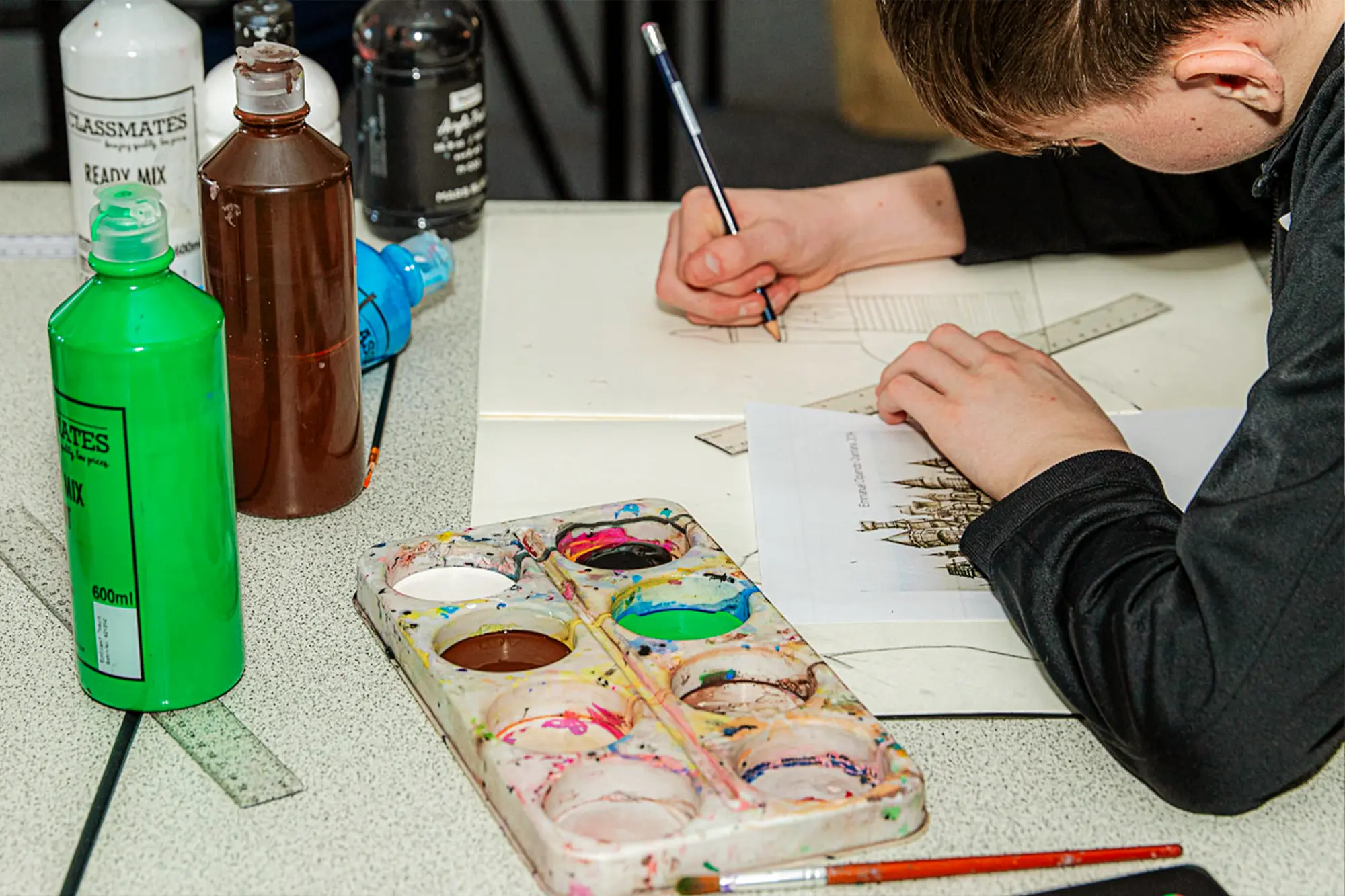 An Egham Park School student sketching a detailed castle drawing with paint and rulers on the table.